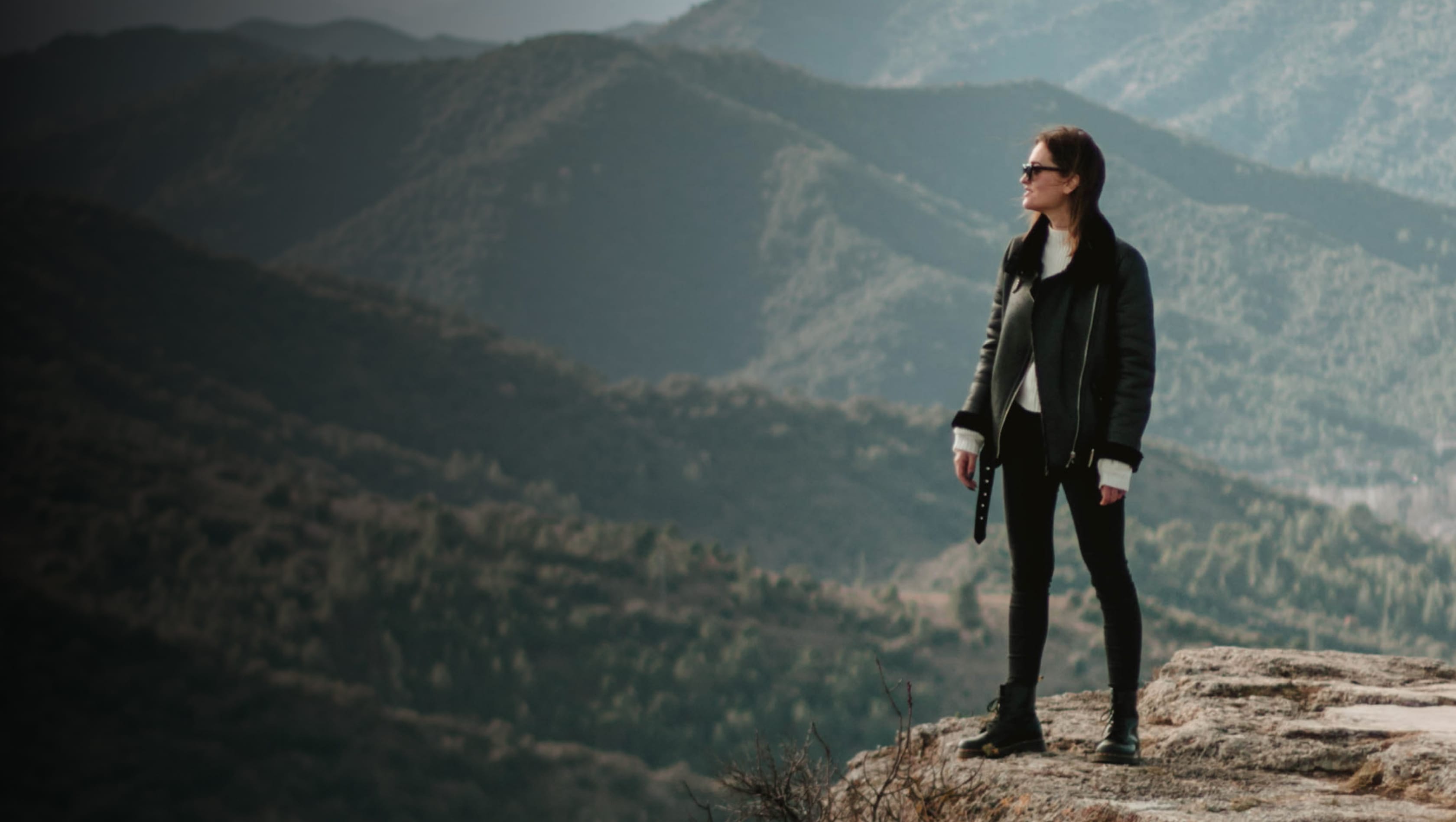 there is a woman standing on a mountain top looking at the mountains