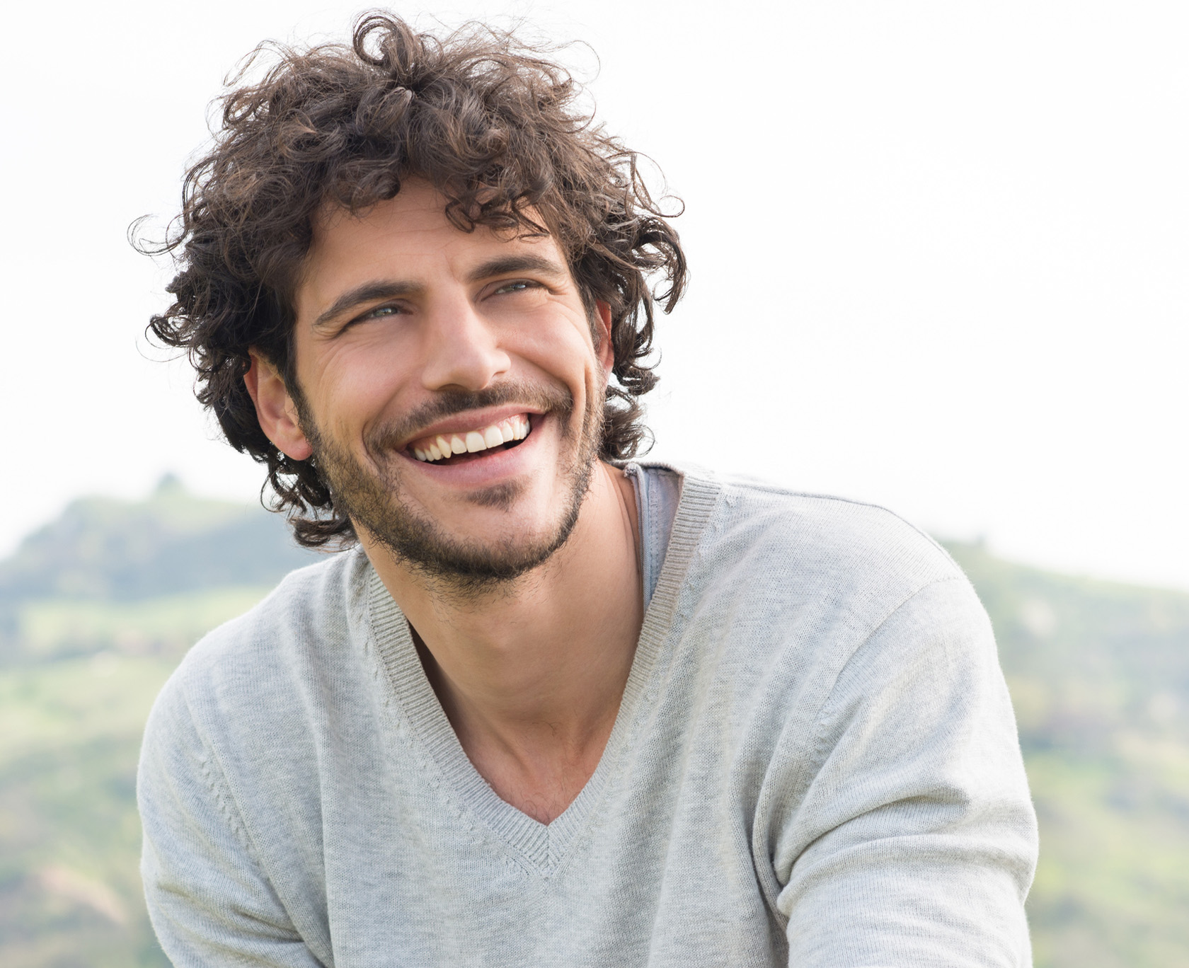 smiling man with curly hair and beard sitting on a hill