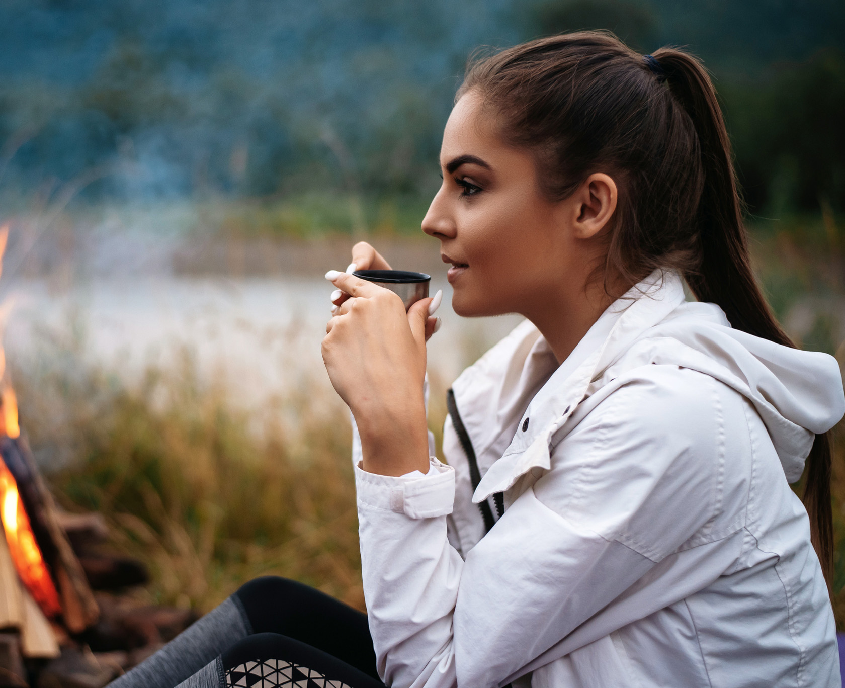 there is a woman sitting by a fire with a cup